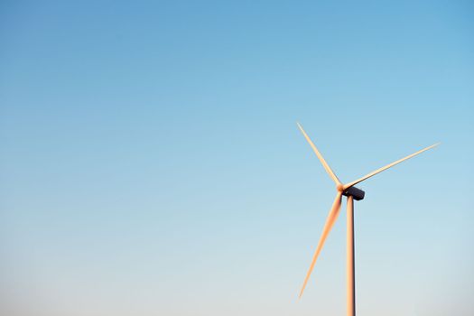 Blades of a windmill isolated on a clean and crystalline blue sky, production of wind energy in an ecological and sustainable way. Copy space