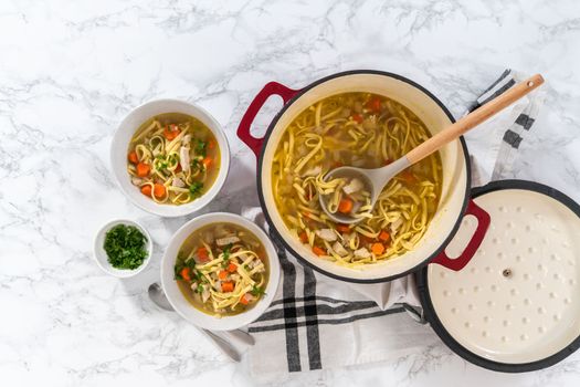 Flat lay. Serving chicken noodle soup with kluski noodles in white ceramic soup bowls.