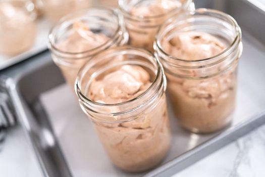Scooping mixture into the small glass jars to make homemade chocolate ice cream.