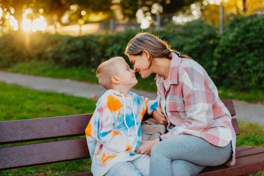 mother and son sit on a park bench in the rays of the setting sun. the concept of a family. Mother's Day. beautiful girl (mother) with a boy (son) in the park in the park are sitting on a bench at sunset.