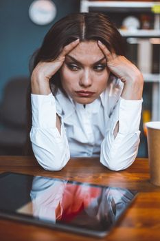 Exhausted business woman sits at workplace taking head in hands. Tired or bored female employee feels stress. Disappointment concept. Tinted image.