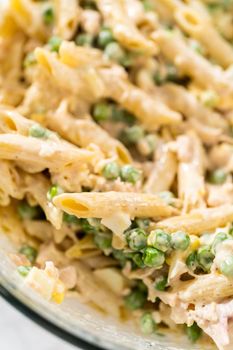 Mixing ingredients in a large glass mixing bowl to make macaroni salad with chicken.