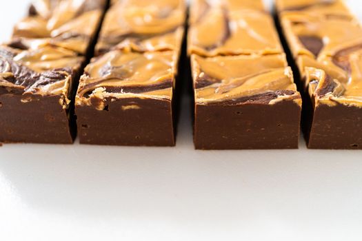 Cutting chocolate fudge with peanut butter swirl into small pieces on a white cutting board.