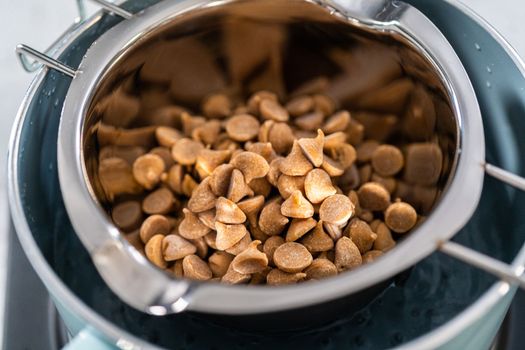 Melting chocolate chips and other ingredients in a glass mixing bowl over boiling water to prepare chocolate fudge with peanut butter swirl.
