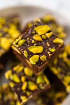 Homemade chocolate pistachio fudge square pieces on a white plate.