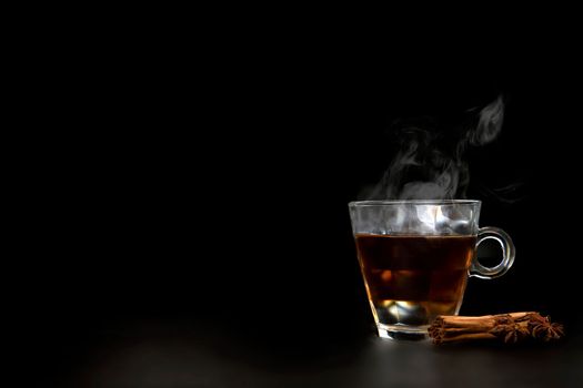 A glass of freshly brewed black tea,escaping steam,warm soft light, darker background. copy space healthy