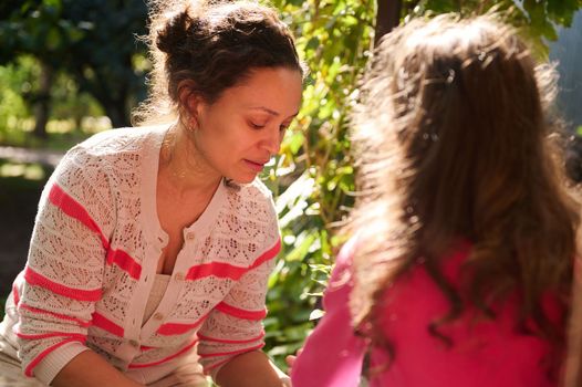 Portrait of beautiful loving mother and her little daughter, enjoying gardening together, planting seedlings in an early spring day at beautiful sunset. Agriculture. Gardening. Eco farming concept