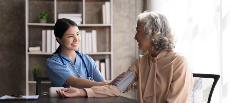 Female nurse doing blood pressure measurement of a senior woman patient. Doctor checking blood pressure of an elderly woman at old age home. Female caregiver and senior woman together at home..