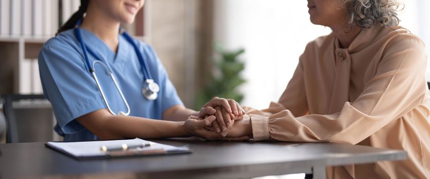 Happy patient is holding caregiver for a hand while spending time together. Elderly woman in nursing home and nurse..