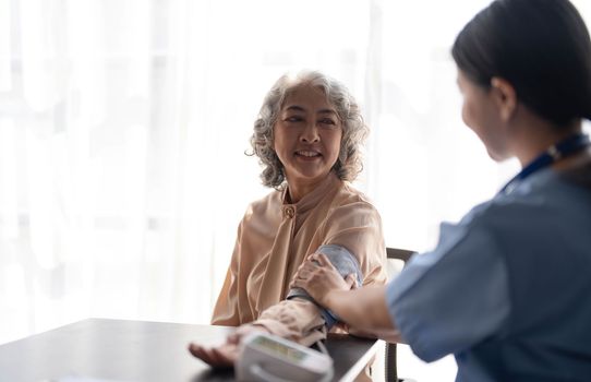 Female nurse doing blood pressure measurement of a senior woman patient. Doctor checking blood pressure of an elderly woman at old age home. Female caregiver and senior woman together at home..