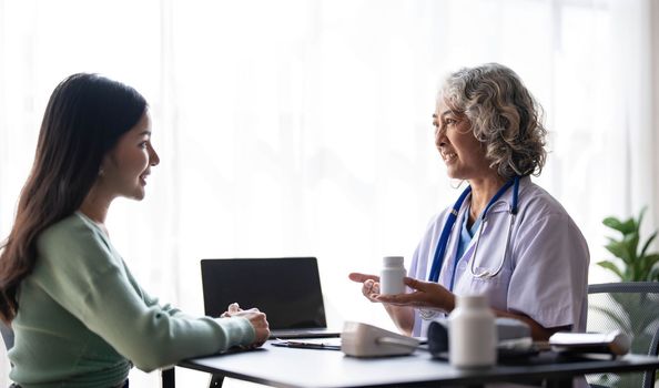 Woman senior doctor is Reading Medical History of Female Patient and Speaking with Her During Consultation in a Health Clinic. Physician in Lab Coat Sitting Behind a Laptop in Hospital Office...