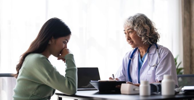 Woman senior doctor is Reading Medical History of Female Patient and Speaking with Her During Consultation in a Health Clinic. Physician in Lab Coat Sitting Behind a Laptop in Hospital Office...