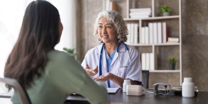 Woman senior doctor is Reading Medical History of Female Patient and Speaking with Her During Consultation in a Health Clinic. Physician in Lab Coat Sitting Behind a Laptop in Hospital Office...