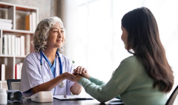 Woman senior doctor is Reading Medical History of Female Patient and Speaking with Her During Consultation in a Health Clinic. Physician in Lab Coat Sitting Behind a Laptop in Hospital Office...