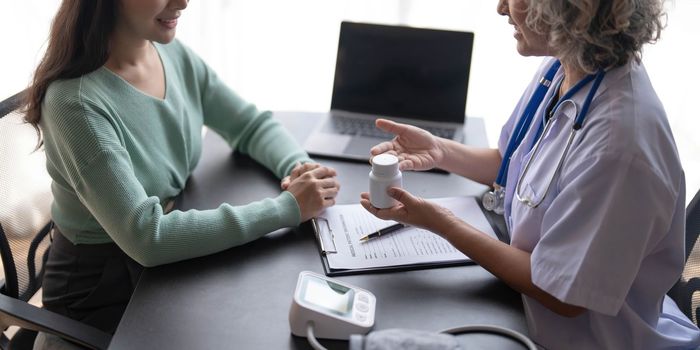 Woman senior doctor is Reading Medical History of Female Patient and Speaking with Her During Consultation in a Health Clinic. Physician in Lab Coat Sitting Behind a Laptop in Hospital Office...