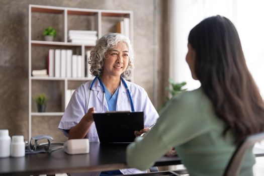 Woman senior doctor is Reading Medical History of Female Patient and Speaking with Her During Consultation in a Health Clinic. Physician in Lab Coat Sitting Behind a Laptop in Hospital Office...