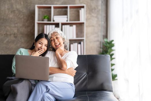 Mature mother grown up daughter sit on couch in living room hold on lap pc looking at screen watching movie film, using device make video call, shopping via e-commerce website, girl teach mom concept..