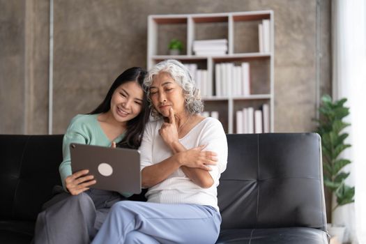 Mature mother grown up daughter sit on couch in living room hold on lap pc looking at screen watching movie film, using device make video call, shopping via e-commerce website, girl teach mom concept..