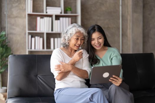 Mature mother grown up daughter sit on couch in living room hold on lap pc looking at screen watching movie film, using device make video call, shopping via e-commerce website, girl teach mom concept..