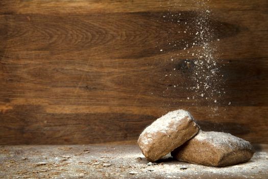 fresh baked whole grain bread on wooden background with falling flour and copy space close up