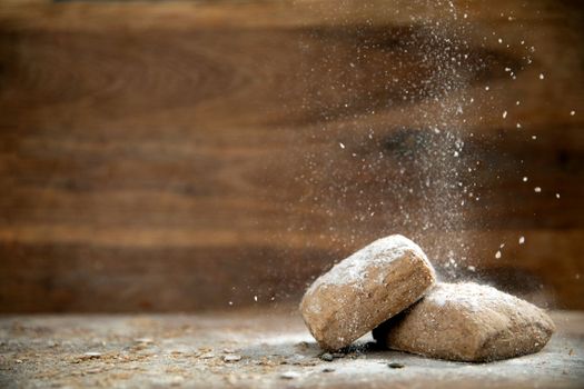 fresh baked whole grain bread on wooden background with falling flour and copy space close up