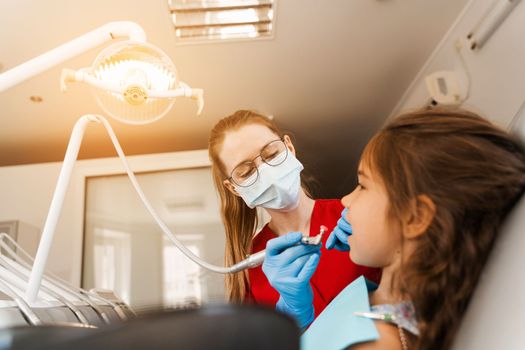 Child dentist makes professional teeth cleaning in dentistry. Professional hygiene for teeth of child in dentistry. Pediatric dentist examines and consults kid patient in dentistry