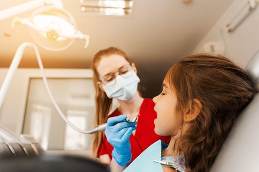 Child dentist makes professional teeth cleaning in dentistry. Professional hygiene for teeth of child in dentistry. Pediatric dentist examines and consults kid patient in dentistry