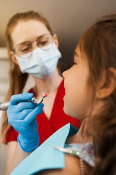 Child dentist makes professional teeth cleaning close-up in dentistry. Professional hygiene for teeth of child in dentistry. Pediatric dentist examines and consults kid patient in dentistry