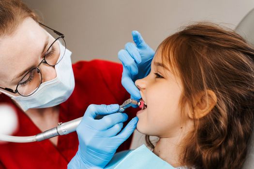 Pediatric girl dentist makes professional teeth cleaning in dentistry. Professional hygiene for teeth of child in dentistry. Pediatric dentist examines and consults kid patient in dentistry