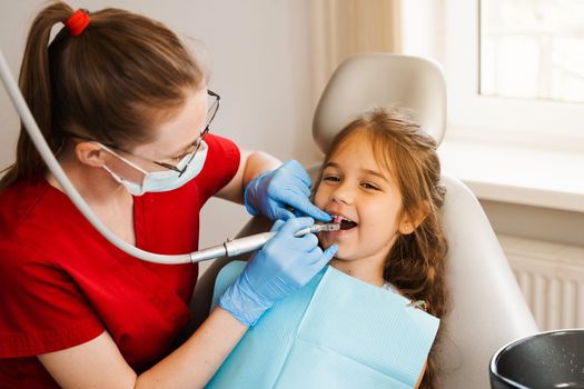 Pediatric girl dentist makes professional teeth cleaning in dentistry. Professional hygiene for teeth of child in dentistry. Pediatric dentist examines and consults kid patient in dentistry