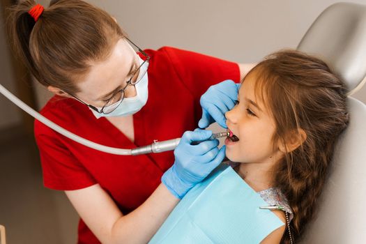 Child dentist makes professional teeth cleaning in dentistry. Professional hygiene for teeth of child in dentistry. Pediatric dentist examines and consults kid patient in dentistry