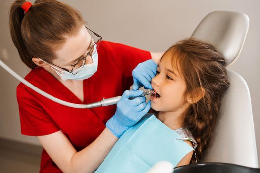 Child dentist makes professional teeth cleaning in dentistry. Professional hygiene for teeth of child in dentistry. Pediatric dentist examines and consults kid patient in dentistry