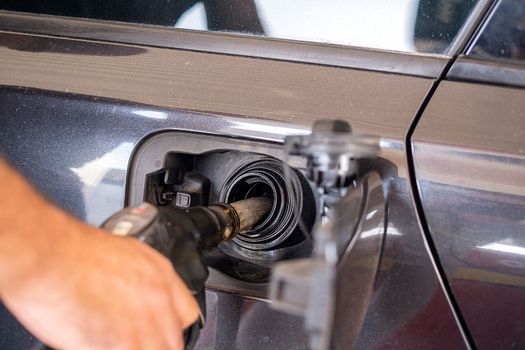 Close up of hand holding gas gun while refueling car with gasoline. Filling fuel into tank of auto at gas station.