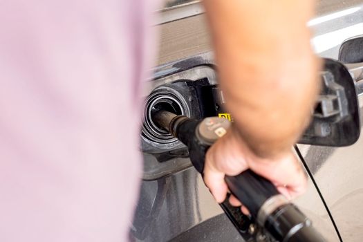 Close up of hand holding gas gun while refueling car with gasoline. Filling fuel into tank of auto at gas station.