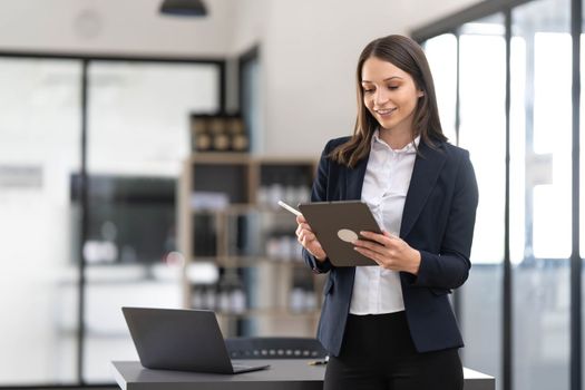 Young asian businesswoman using the tablet to analyze business data while she is standing at the office...