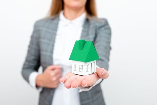 Businesswoman in a gray suit holding a colored paper house in one hand.