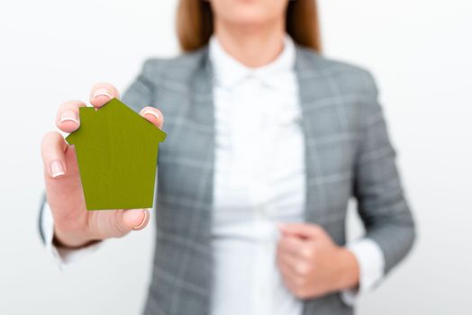 Businesswoman in a gray suit holding a colored paper house in one hand.