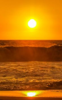 Beautiful stunning colorful and golden sunset in yellow orange red on beach and big wave panorama in tropical nature in Zicatela Puerto Escondido Oaxaca Mexico.