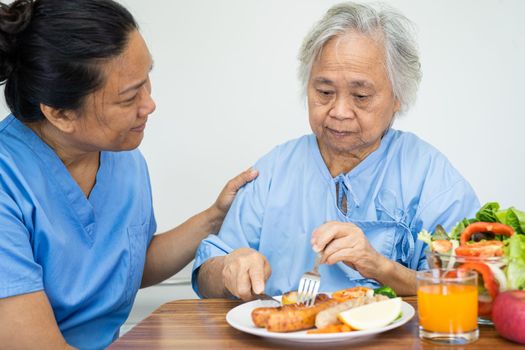 Asian senior or elderly old lady woman patient eating breakfast vegetable healthy food with hope and happy while sitting and hungry on bed in hospital.