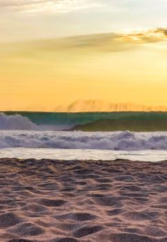 Beautiful stunning colorful and golden sunset in yellow orange red on beach and big wave panorama in tropical nature in Zicatela Puerto Escondido Oaxaca Mexico.