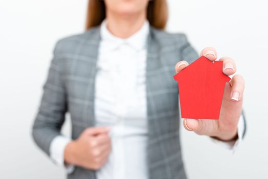 Businesswoman in a gray suit holding a colored paper house in one hand.