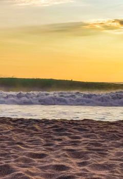 Beautiful stunning colorful and golden sunset in yellow orange red on beach and big wave panorama in tropical nature in Zicatela Puerto Escondido Oaxaca Mexico.