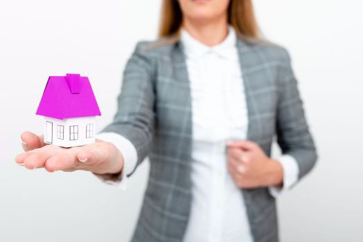 Businesswoman in a gray suit holding a colored paper house in one hand.