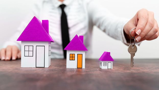 Businesswoman holding keys. olored paper houses standing on desk.