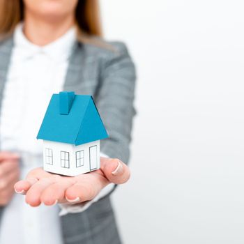 Businesswoman in a gray suit holding a colored paper house in one hand.