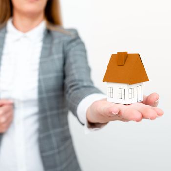 Businesswoman in a gray suit holding a colored paper house in one hand.