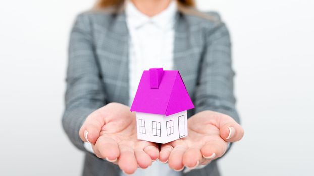 Businesswoman in a gray suit holding a colored paper house in one hand.