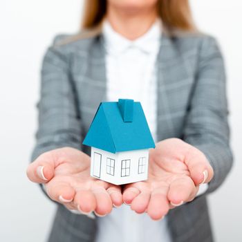 Businesswoman in a gray suit holding a colored paper house in one hand.