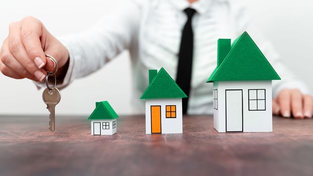 Businesswoman holding keys. olored paper houses standing on desk.