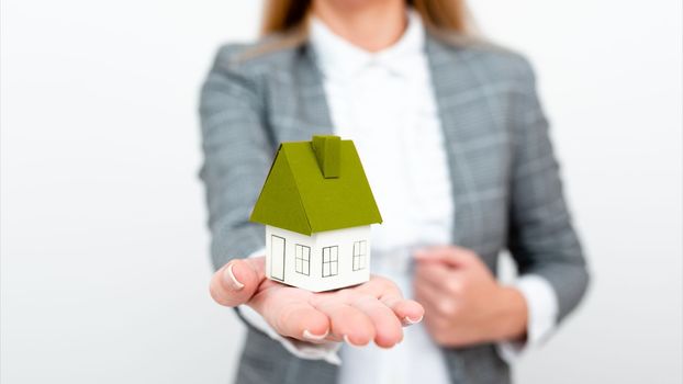 Businesswoman in a gray suit holding a colored paper house in one hand.